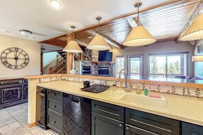A kitchen with a large island, wooden ceiling beams, pendant lights, a stone fireplace, and a clock on the wall. - Gorgeous Townhouse w/Free WiFi, Private Washer/Dryer, Lake Views - Near Keystone (Dillon)