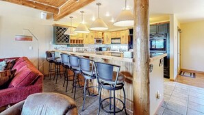 Une cuisine avec des poutres en bois, un coin bar avec des tabourets et une table à manger.