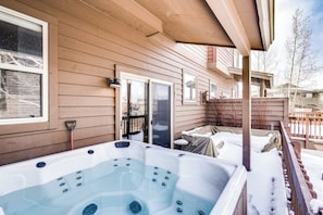 Ein Whirlpool auf einer Holzterrasse mit überdachtem Bereich, einer Schiebetür und einem Holzzaun.