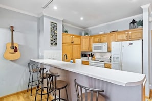 Eine Küche mit Holzausstattung, einer weißen Arbeitsplatte, einem weißen Kühlschrank und einer Gitarre an der Wand.