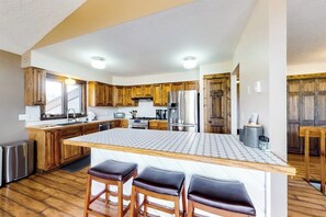 Eine Küche mit Holzausbau, einem Edelstahlkühlschrank, einer großen Kochinsel mit Hockern und einem eingebauten Backofen.