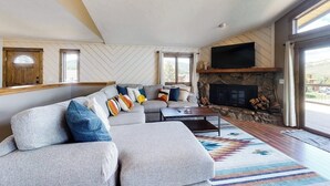 Een moderne woonkamer met een hoekbank, een open haard en grote ramen.