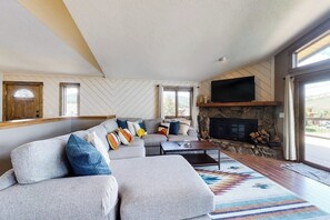 Ein modernes Wohnzimmer mit einer Eckcouch, einem Kamin und großen Fenstern.