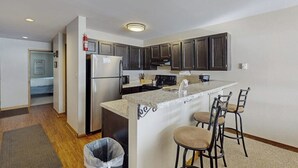 Una cucina compatta con mobili scuri, un frigorifero, un piano cottura e un angolo bar con sgabelli.