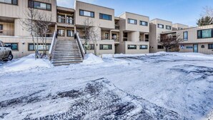 Un edificio a più piani con una scalinata centrale, unità a tetto piatto e un'area di parcheggio coperta di neve.