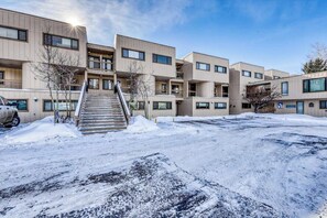 A multi-story building with a central staircase, flat-roofed units, and a parking area covered in snow. - Lake & ski view condo | Pool, hot tub, sauna & cozy fireplace (Dillon)