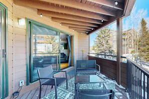 Eine Holzterrasse mit Gartenmöbeln, eine Glastür, die zu einem Innenbereich führt, und Blick auf eine Wohngegend mit Bäumen und Gebäuden.