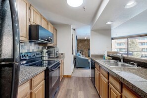Eine moderne Küche mit Holzausstattung, einer schwarzen Dunstabzugshaube, einem eingebauten Ofen und einer Arbeitsplatte aus Granit.