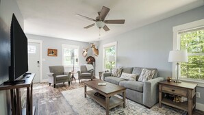Ein Wohnzimmer mit Fernseher, zwei Sofas, einem Couchtisch, einem Deckenventilator und einem großen Fenster.