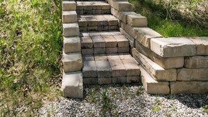 Ein Haus mit einer Steintreppe, die davor hochführt, umgeben von Bäumen und Grün.