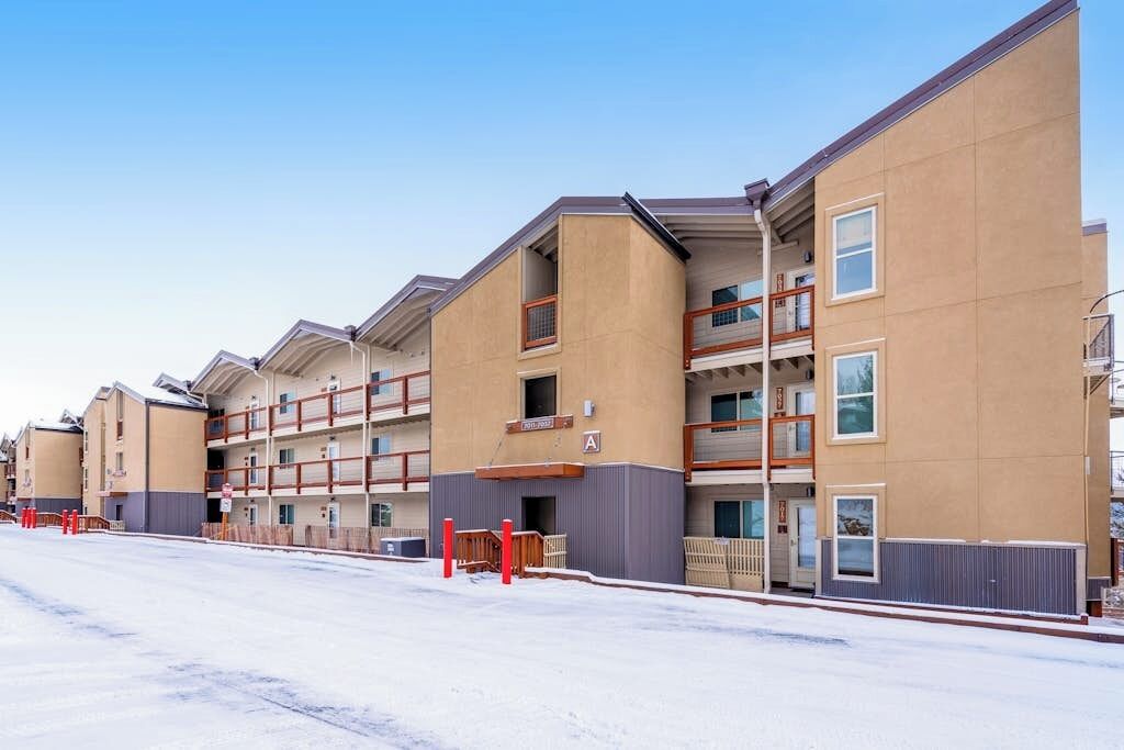 Une rangée d’immeubles à plusieurs étages, dotés de balcons, avec une entrée fermée par un portail et un sol recouvert de neige.