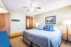 Ein Schlafzimmer mit einem Bett, Deckenventilator, Holztür und einem gerahmten Bild an der Wand.