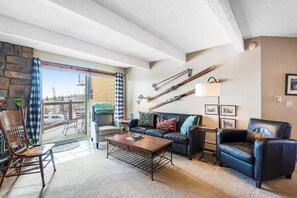 Ein gemütliches Wohnzimmer mit Steinwand, einer Couch, einem Couchtisch, einem Sessel und Blick durch eine Schiebetür auf einen Außenbereich.