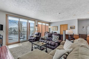Ein großzügiger Wohnraum mit einer großen Schiebeglastür, die auf einen Balkon führt, mit Ledersofas, einem Couchtisch und einem Essbereich.