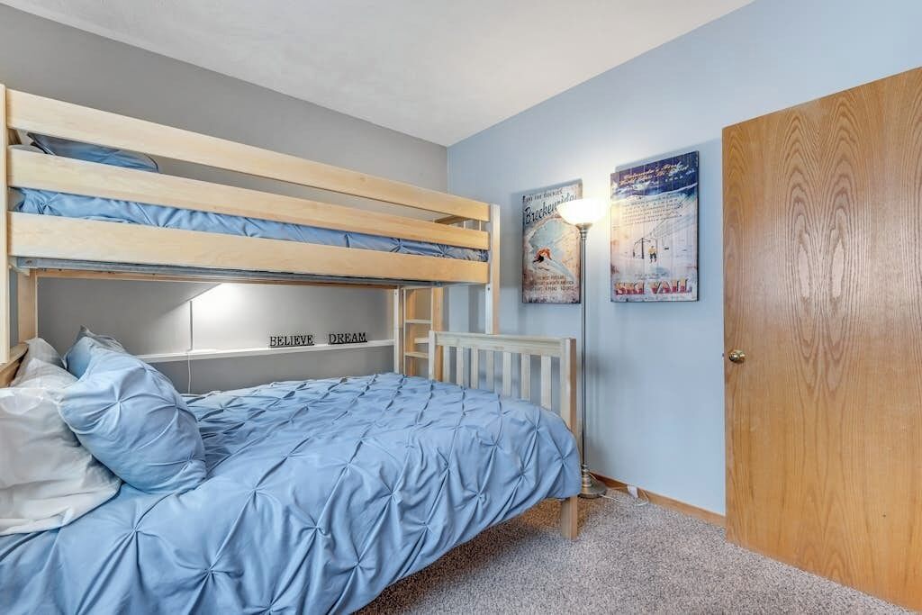 Dormitorio con literas, una colcha azul, una puerta de madera y dos carteles colgados en las paredes.