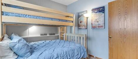 Dormitorio con literas, una colcha azul, una puerta de madera y dos carteles colgados en las paredes.