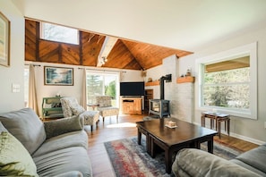 A living room with a high ceiling, a fireplace, a television, and a large window.
