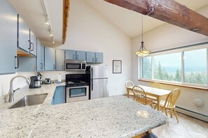 A kitchen with granite countertops, a dining area with a table and chairs, and a large window with a view. - Top-floor w/ Mountain View (Silverthorne)