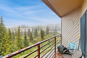 A balcony with a view of a forested area, a chair, and a railing. - Top-floor w/ Mountain View (Silverthorne)