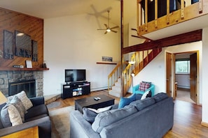 A spacious living area with a stone fireplace, a television, a sofa, and a staircase. - Top-floor w/ Mountain View (Silverthorne)