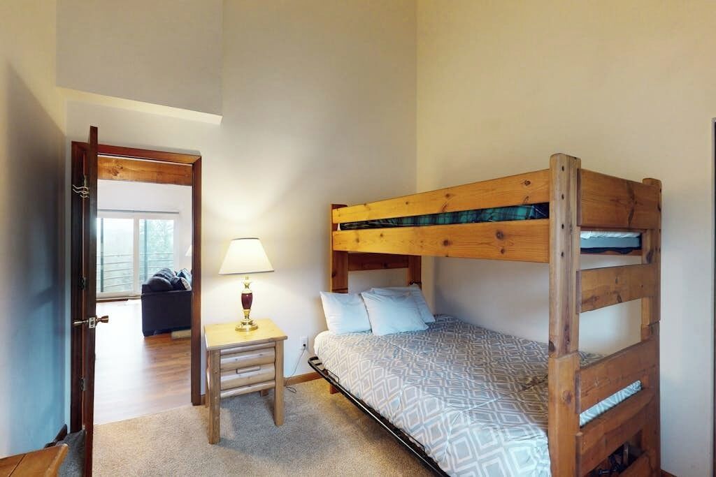 A bunk bed with a wooden frame, a bedside table with a lamp, and a patterned bedspread.