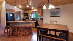 Una cocina con armarios de madera, un refrigerador, un microondas y un comedor con mesa y sillas de madera.