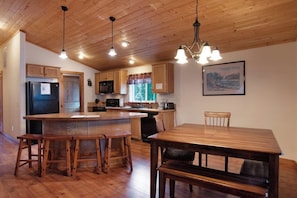 A kitchen with wooden cabinets, a refrigerator, a microwave, and a dining area with a wooden table and chairs. - Waterfront cabin with private hot tub, furnished deck, wood stove, & free WiFi (South Fork)