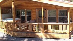 Una cabaña de madera con terraza cubierta, jacuzzi y zona de barbacoa.