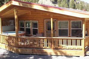 A wooden cabin with a covered deck, a hot tub, and a grill area. - Waterfront cabin with private hot tub, furnished deck, wood stove, & free WiFi (South Fork)