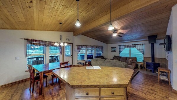 A spacious living area with a large wooden dining table, a sofa, and a fireplace. - Waterfront cabin with private hot tub, furnished deck, wood stove, & free WiFi (South Fork)