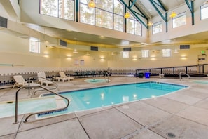Ein großes Hallenbad mit Liegestühlen, einer Whirlpool-Anlage und einer hohen Decke mit Tageslicht.