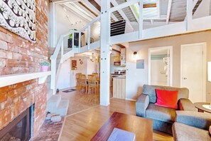 Ein geräumiges Loft mit Kamin aus Backstein, einem Essbereich, einer Küche und einem Wohnzimmer mit Sofa und Couchtisch.