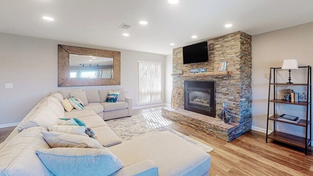 A modern living room with a stone fireplace, a large sofa, a television, and a bookshelf. - Mountain View Condo with Private Balcony, Gas Fireplace & Free WiFi (Silverthorne)
