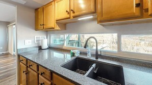 A kitchen with wooden cabinets, a granite countertop, a stainless steel sink, and a window with a view. - Mountain View Condo with Private Balcony, Gas Fireplace & Free WiFi (Silverthorne)