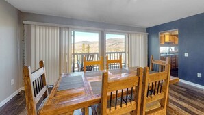 A dining area with a wooden table and chairs, large windows with blinds, and a view of the outdoors. - Mountain View Condo with Private Balcony, Gas Fireplace & Free WiFi (Silverthorne)