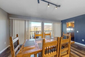 Ein Essbereich mit Holztisch und Stühlen, großen Fenstern mit Jalousien und Blick ins Freie.