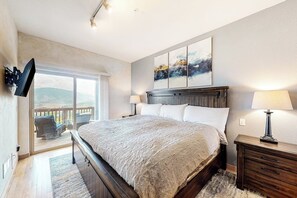 A bedroom with a large bed, a TV mounted on the wall, a balcony with outdoor furniture, and a painting above the bed. - Mountain view home with high-speed WiFi and washer/dryer (Silverthorne)