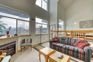 Ein geräumiges Wohnzimmer mit Kamin, großen Fenstern, einer Couch und einem Essbereich.