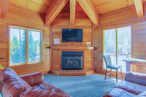 Ein Blockhaus-Interieur mit Kamin, Fernseher und einer Couch.