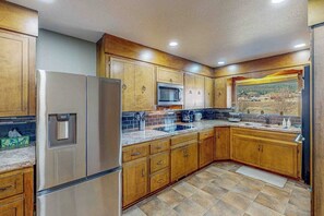 A kitchen with wooden cabinets, a stainless steel refrigerator, a microwave, and a sink. - Spacious cabin with river views, private hot tub, sun room, and full kitchen! (South Fork)