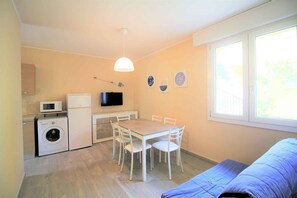 Ein kompakter Wohnraum mit Essbereich, Waschmaschine, Fernseher und einem großen Fenster.