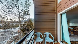 Uma varanda com duas cadeiras, um deck de madeira e vista para uma paisagem nevada.