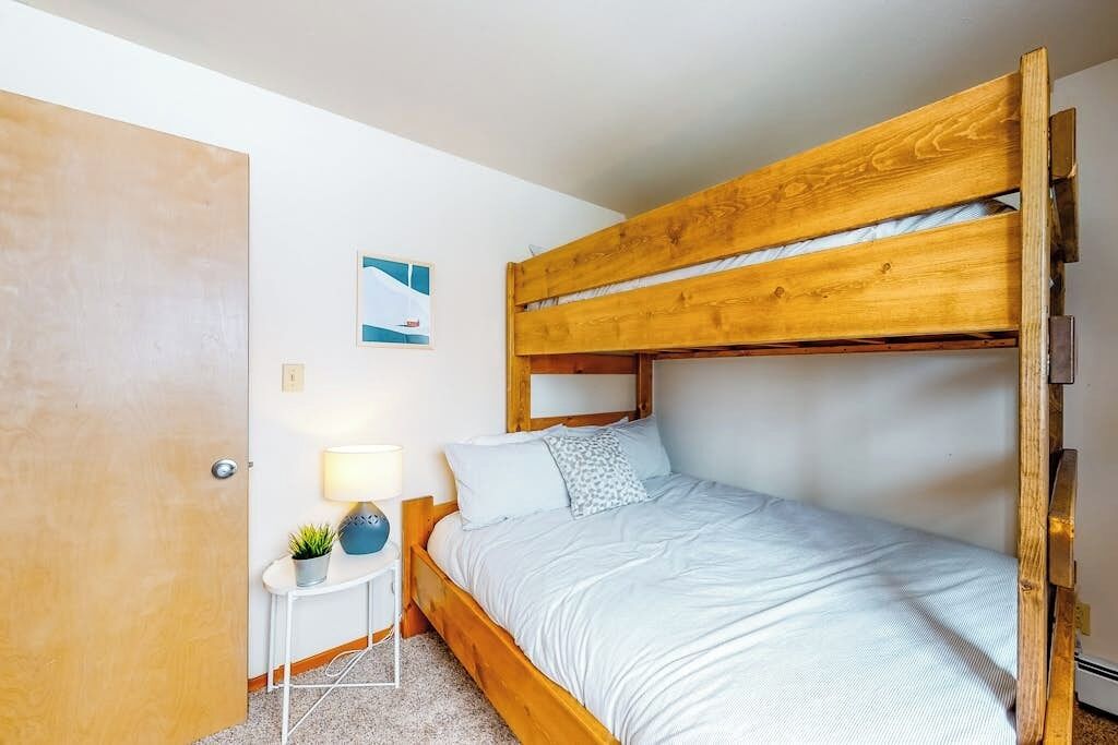 Een enkel bed met houten hoofdbord in een kamer met een klein nachtkastje, een lamp en een aan de muur hangend schilderij.