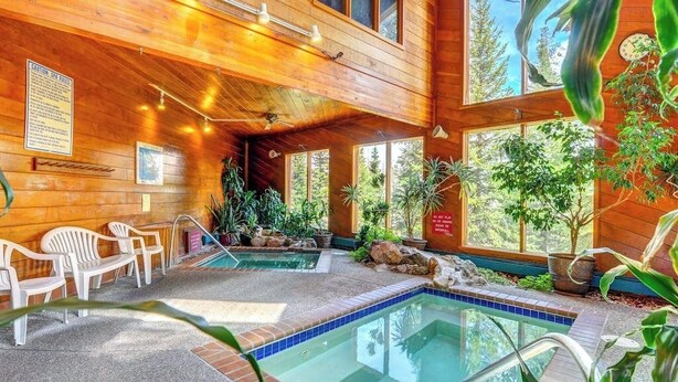 Uma cabana de madeira com piscina, cadeiras brancas e plantas em vasos.