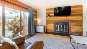 Uma sala de estar moderna com lareira, TV de tela plana e vista para o exterior.