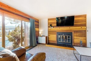 Ein modernes Wohnzimmer mit Kamin, Flachbildfernseher und Blick ins Grüne.