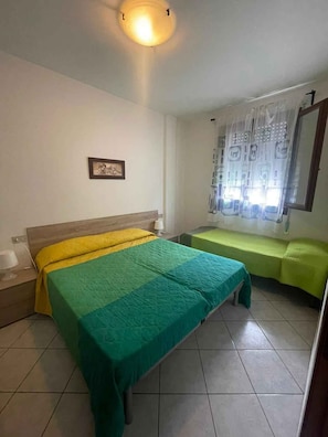 A room with a bed, a bench, a wall-mounted picture, and a window with curtains. - Holiday apartment with air conditioning and balcony (Rosolina Mare)