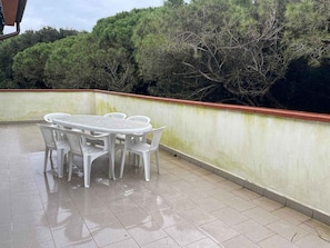 A patio with a round table and chairs, a tiled floor, and a low wall with trees in the background. - Holiday apartment with air conditioning and balcony (Rosolina Mare)