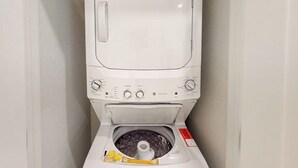 Una lavadora blanca con panel de control, dispensador de detergente y una etiqueta de seguridad roja.