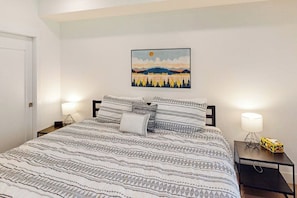 Ein ordentlich bezogenes Bett mit gemusterten Bettwäsche, ein an der Wand hängendes Bild und Nachttischlampen auf einem Nachttisch.